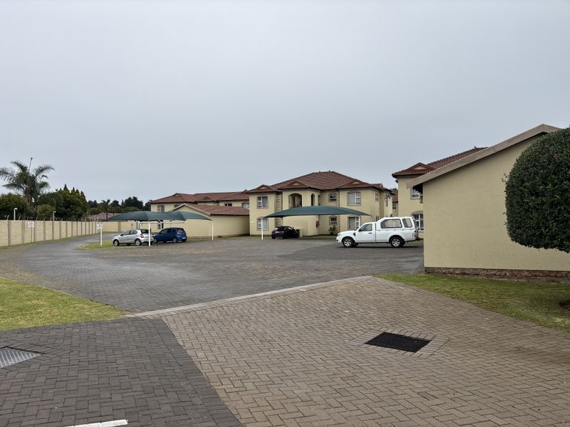 Exterior view of a townhouse complex featuring a large paved parking area with shade cloth carports and well-maintained building facades.