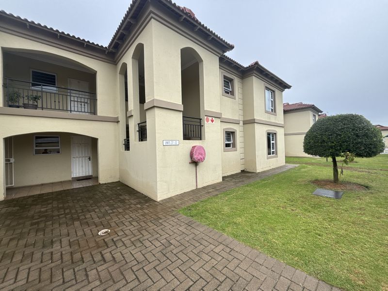 Exterior view of a multi-story townhouse complex featuring paved driveway access, covered balconies, and well-maintained communal lawn areas.