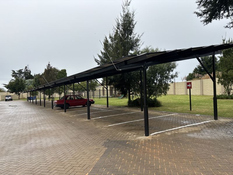 A covered carport area with paved parking bays and a perimeter wall, situated within a residential complex.