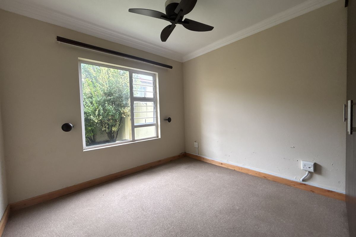 A vacant bedroom featuring neutral walls, carpeted flooring, a ceiling fan, and built-in cupboard storage.