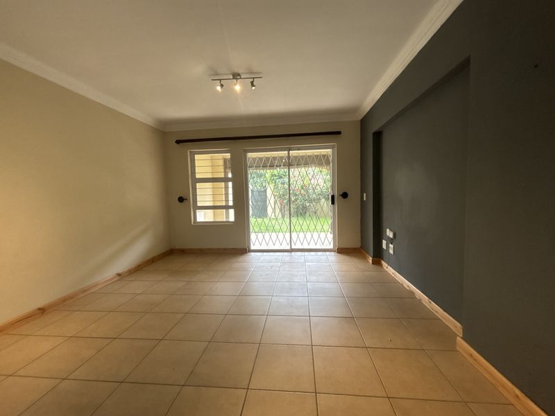 An empty living room featuring tiled flooring, coving, and a sliding glass door with a security gate leading to the garden.