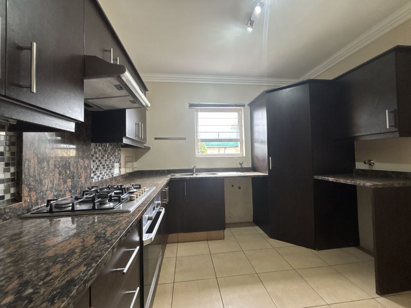 A functional kitchen featuring dark built-in cabinetry, granite countertops, a gas hob with extractor, and tiled flooring in a clean, empty space.