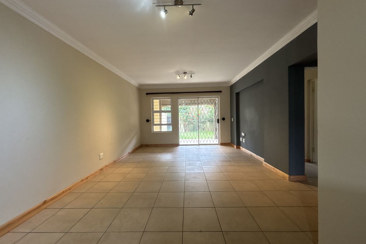 Spacious, empty living area featuring neutral tiled flooring, modern track lighting, and a sliding glass door with security gate leading to the rear garden.