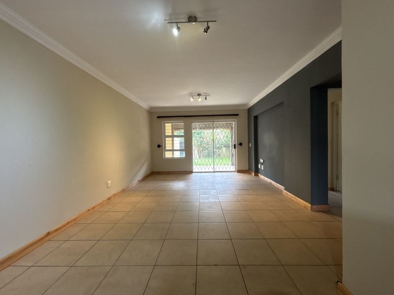 Spacious, empty living area featuring neutral tiled flooring, modern track lighting, and a sliding glass door with security gate leading to the rear garden.