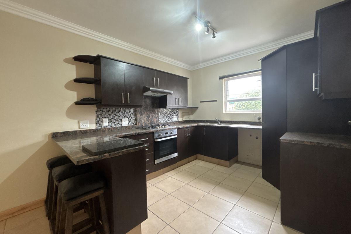 A functional kitchen featuring dark wood cabinetry, laminate countertops, a built-in oven with gas hob, and a breakfast bar area.