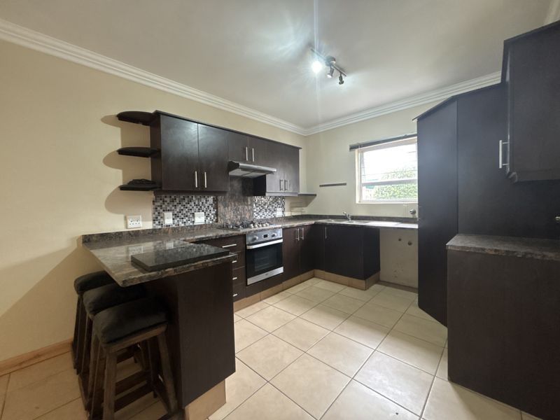 A functional kitchen featuring dark wood cabinetry, laminate countertops, a built-in oven with gas hob, and a breakfast bar area.