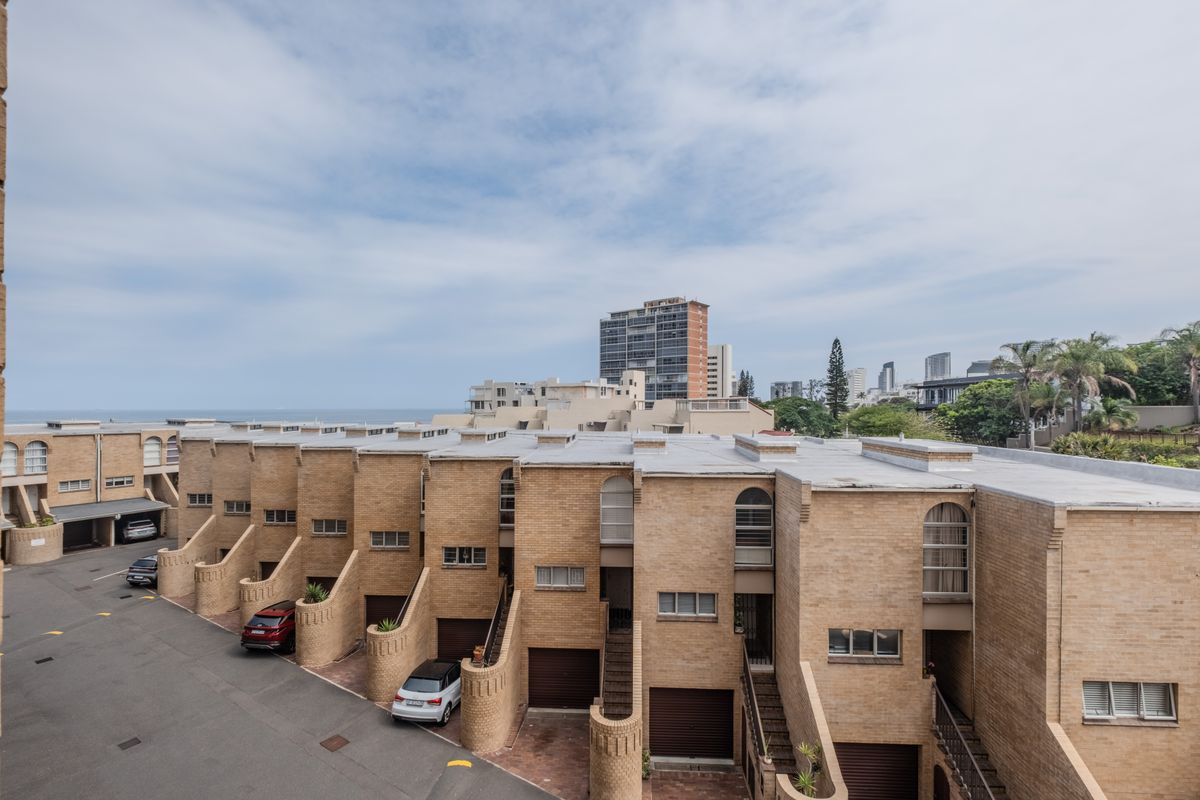 Elevated aerial view of a residential apartment complex featuring brick facades, integrated garages, and external staircases with a coastal city backdrop.