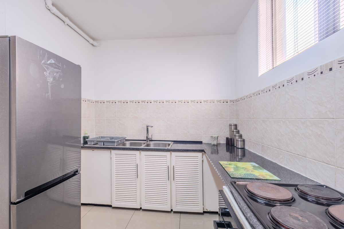 Compact kitchen featuring granite countertops, a stainless steel double sink, electric hob, and louvered cabinetry with tiled backsplash.