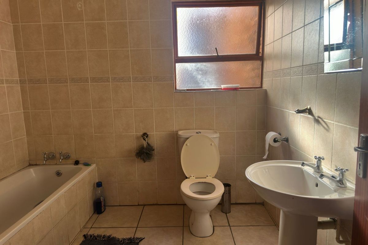 A functional bathroom featuring a bathtub, pedestal basin, and toilet with neutral wall and floor tiling.