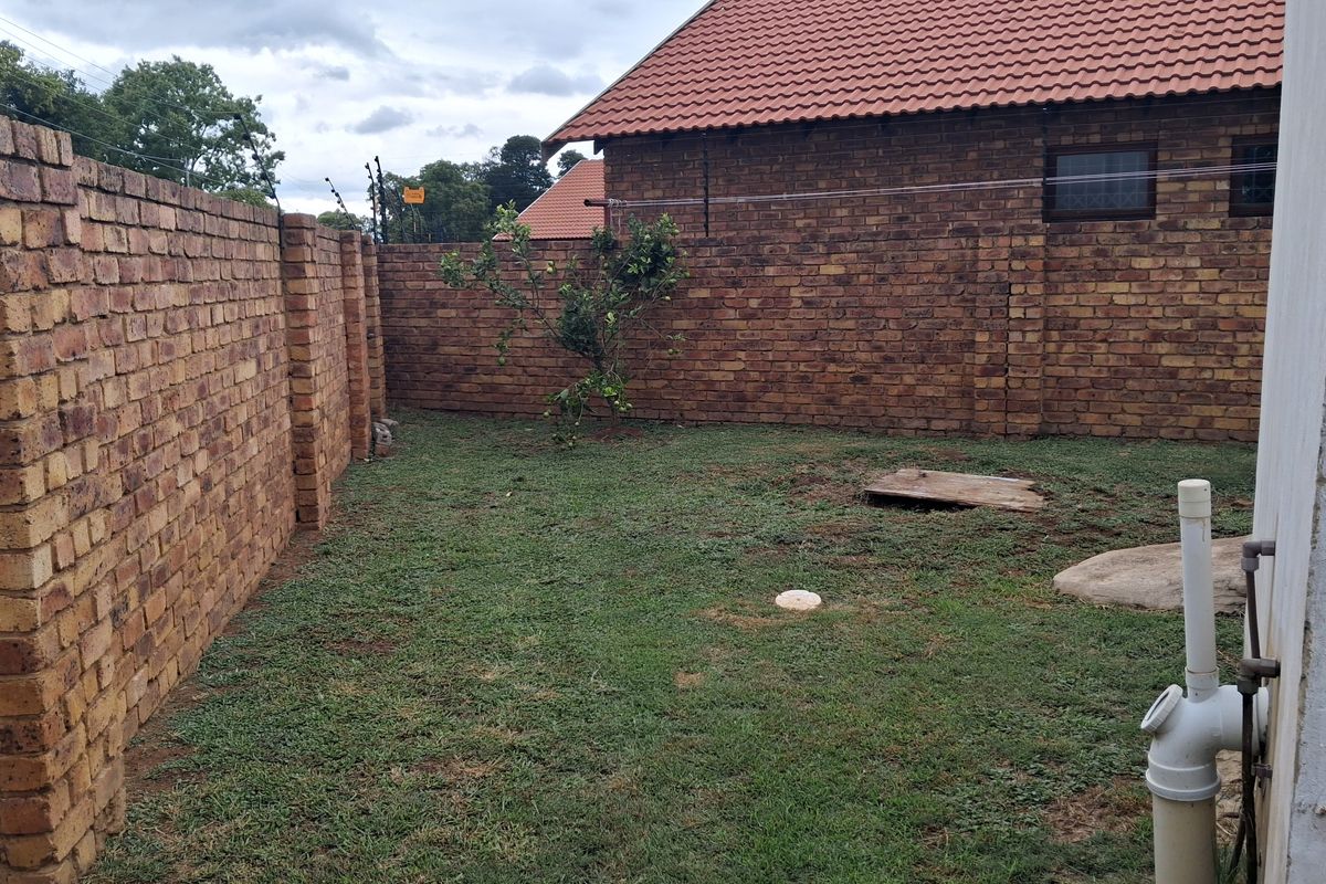 A private rear garden area featuring face brick boundary walls with electric fencing and a tiled roof structure visible in the background.