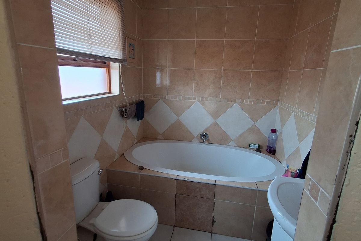 A functional bathroom featuring a built-in bathtub, pedestal basin, toilet, and neutral ceramic wall tiling.