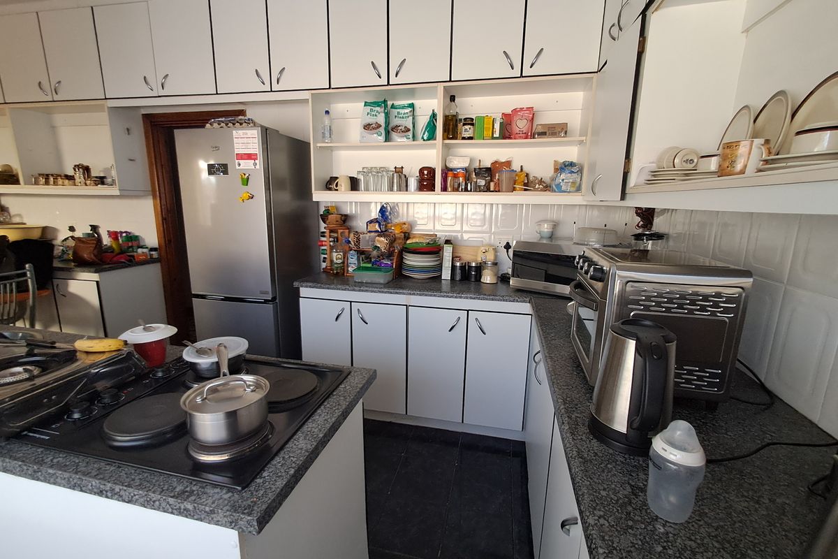 A functional kitchen featuring white cabinetry, granite countertops, a tiled backsplash, and a central island with an integrated electric hob.
