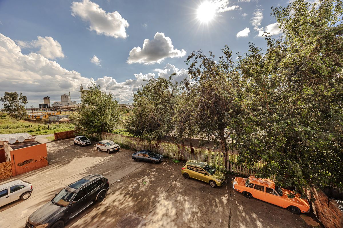 An elevated view of the property's exterior parking area, featuring concrete paving, perimeter fencing, and surrounding mature trees.