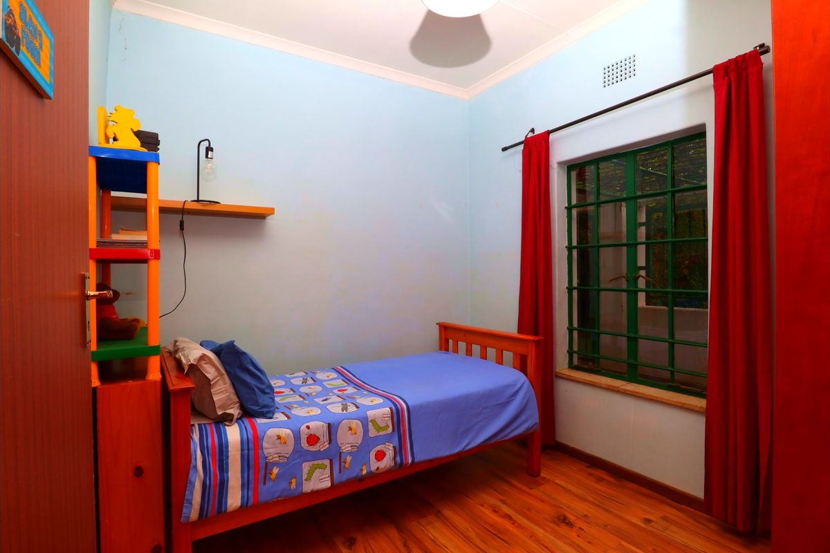 A standard bedroom featuring wooden flooring, a window with security bars, and neutral wall finishes.