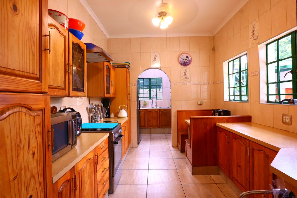 A traditional kitchen featuring wooden cabinetry, tiled finishes, a built-in breakfast nook, and an adjoining scullery area accessible through an archway.