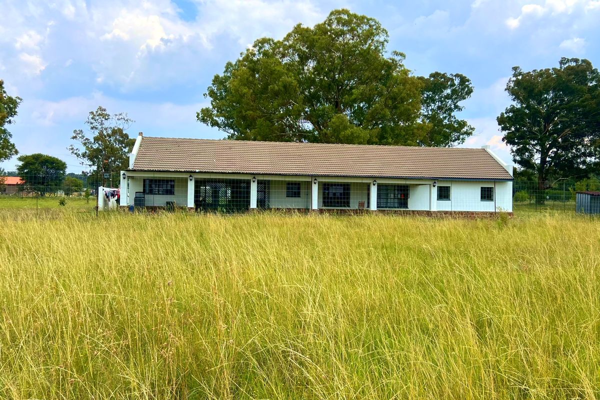 A rear view of a single-story farmhouse featuring a covered patio, tiled roof, and surrounding open field landscape.