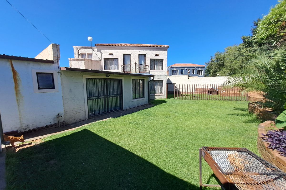 Rear view of the townhouse featuring a private garden, lawn area, and a balcony accessible from the upper level.