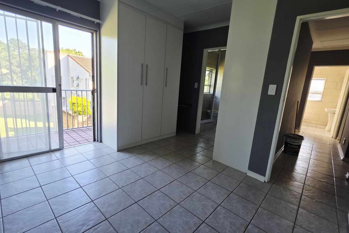 An empty bedroom featuring tiled flooring, built-in cupboards, and a sliding glass door providing access to a private balcony.