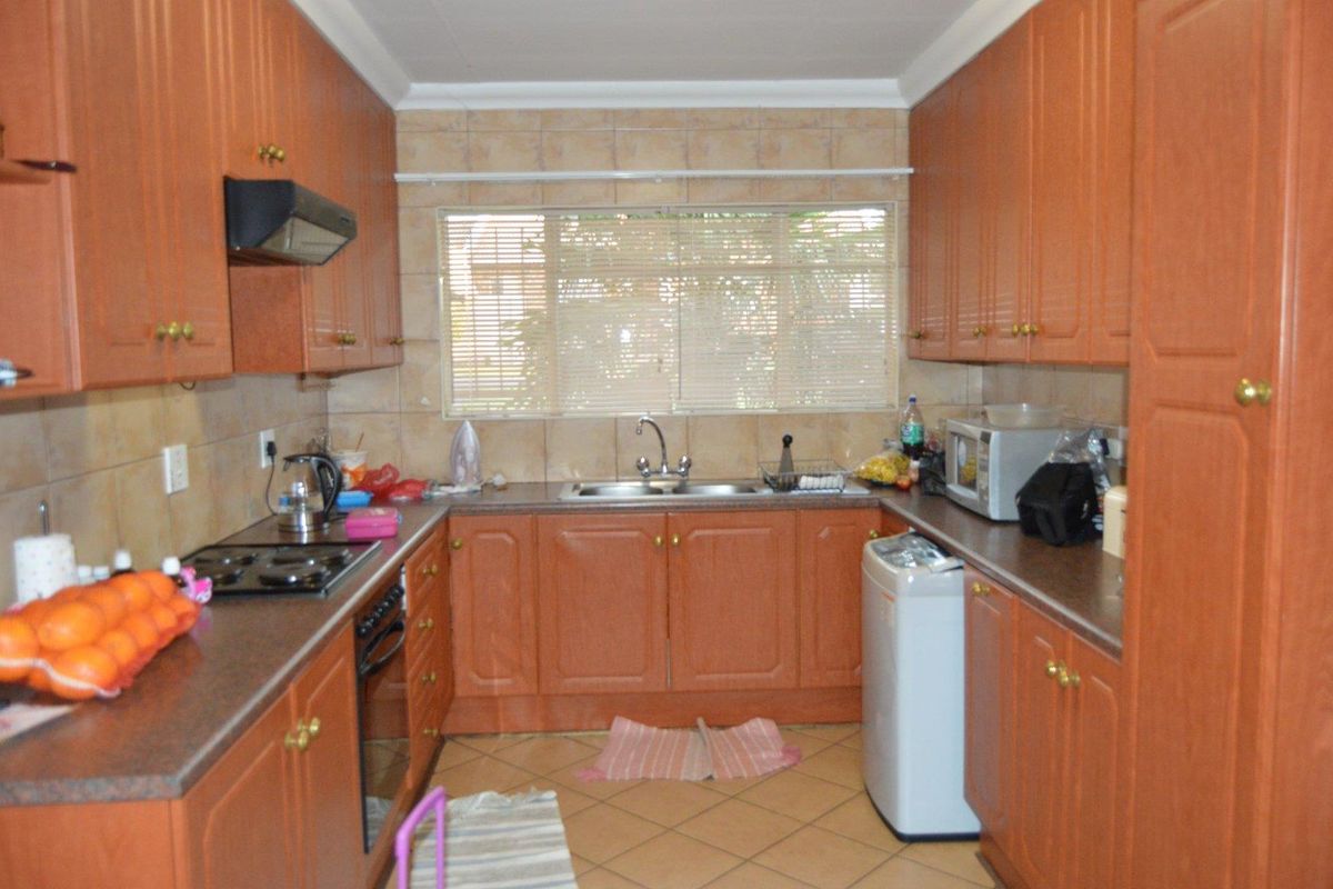 A functional galley-style kitchen featuring wood-finish cabinetry, tiled splashbacks, a built-in hob, oven, and extractor fan with a double sink.