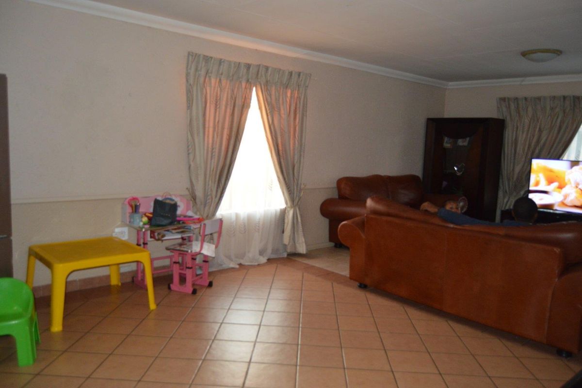 A spacious living room featuring tiled flooring, neutral wall tones, and large windows with curtains, providing a comfortable and functional family living area.