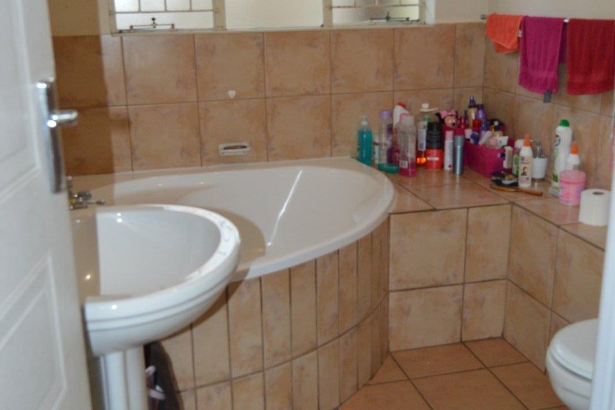 A functional bathroom featuring a corner bathtub, pedestal basin, and tiled flooring with neutral wall tiling.