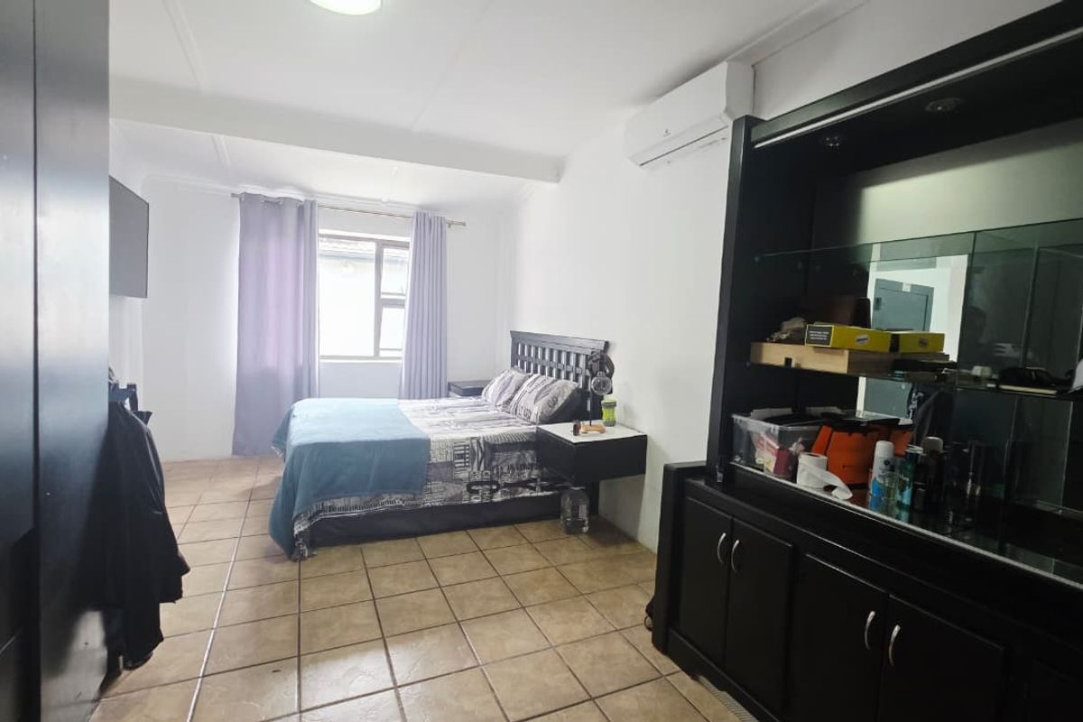 Spacious bedroom featuring tiled flooring, a wall-mounted air conditioning unit, and built-in cabinetry, offering a functional layout with natural light.