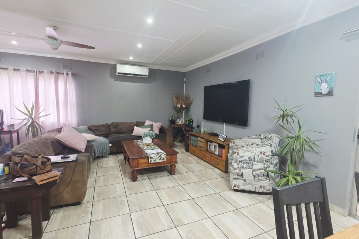 A spacious living room featuring tiled flooring, a ceiling fan, and a wall-mounted split-system air conditioner.