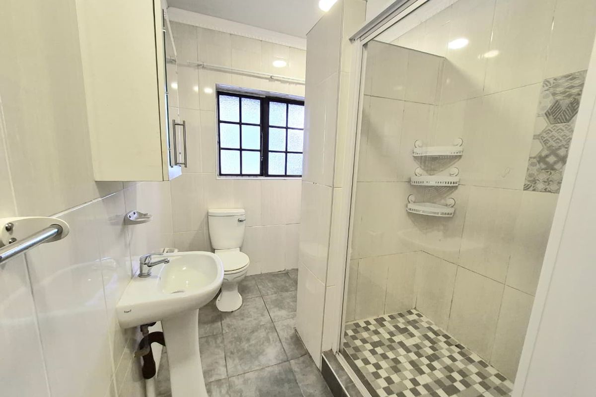 A functional bathroom featuring a pedestal washbasin, toilet, and a separate shower enclosure with tiled walls and flooring.