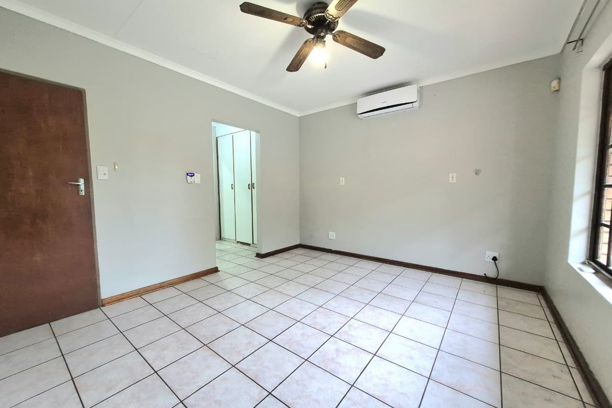 An empty bedroom featuring tiled flooring, a ceiling fan, and a wall-mounted air conditioning unit, with access to built-in storage.