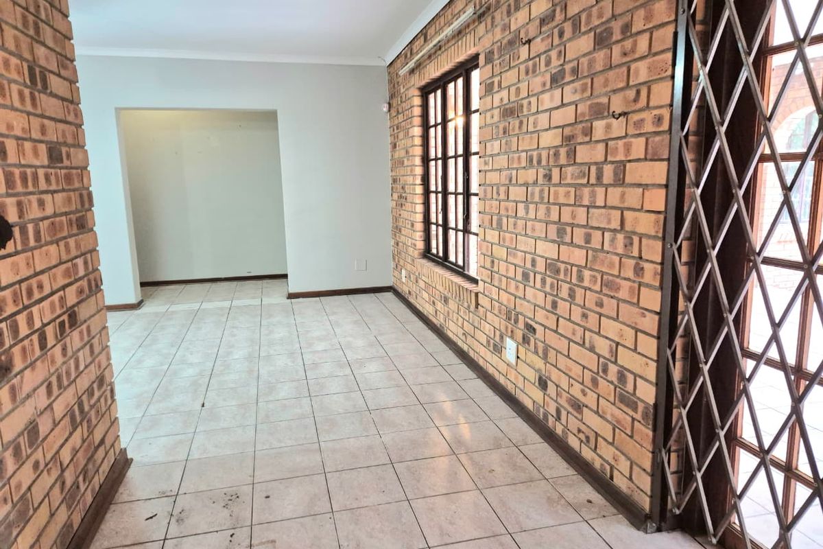 An empty living area featuring exposed brick walls, ceramic tiled flooring, and a security gate leading to the exterior.