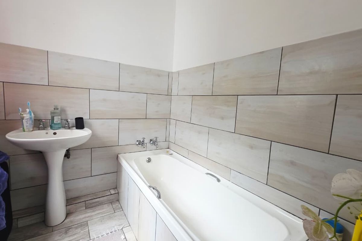 A clean bathroom featuring a white pedestal basin and a built-in bathtub with neutral-toned ceramic wall and floor tiles.