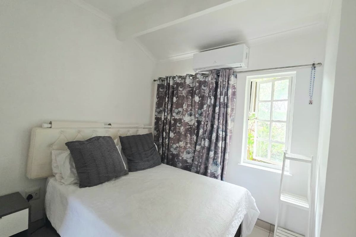 A compact bedroom featuring a wall-mounted air conditioning unit, tiled flooring, and a casement window allowing natural light.