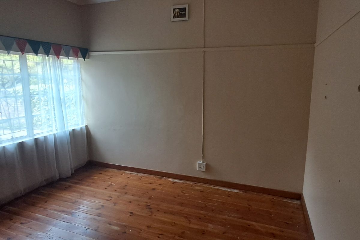 An empty bedroom featuring original timber flooring, large windows with security bars, and neutral wall finishes.
