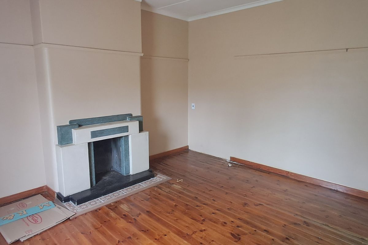 An empty living room featuring original timber flooring, a character fireplace, and picture rails, offering a blank canvas for renovation.