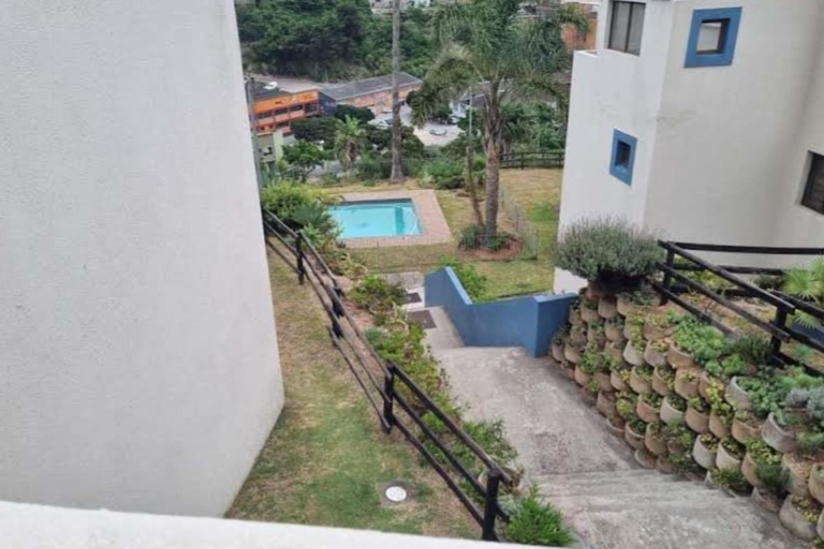 Elevated view of the rear garden area featuring a swimming pool, concrete staircase, and tiered retaining walls with established landscaping.