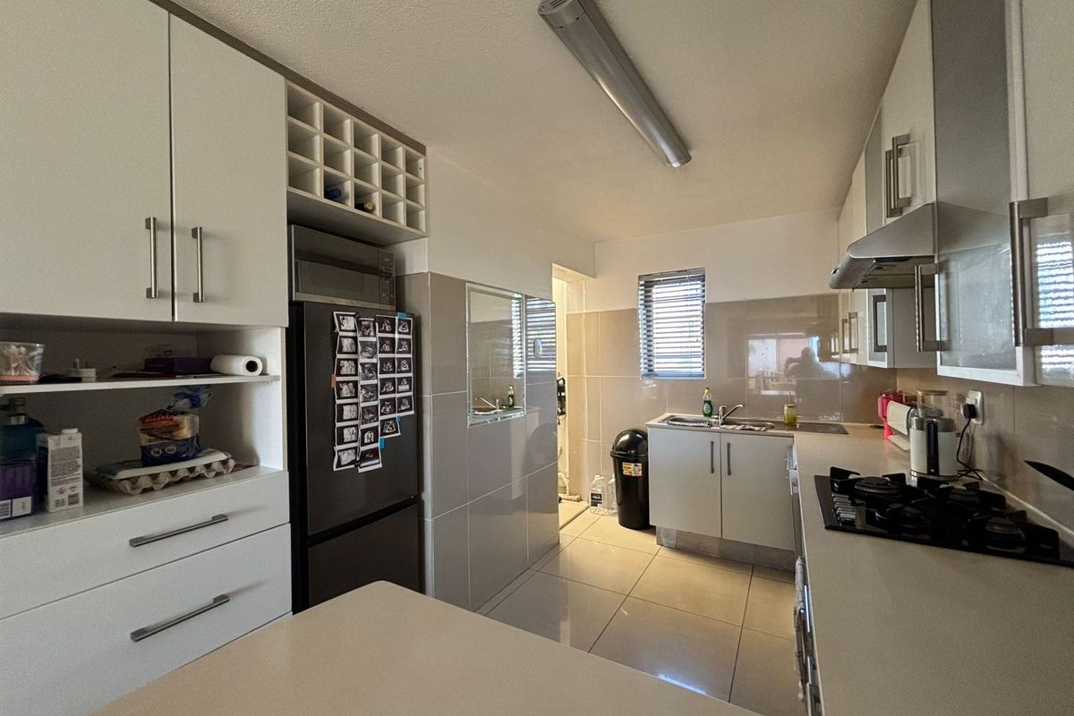 Functional kitchen featuring white cabinetry, tiled splashbacks, gas hob with extractor fan, and tiled flooring, offering a clean and practical workspace.