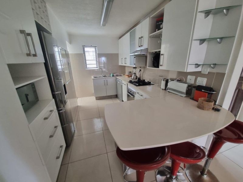A functional kitchen featuring white cabinetry, a gas hob, integrated oven, tiled splashbacks, and a convenient breakfast counter for casual dining.
