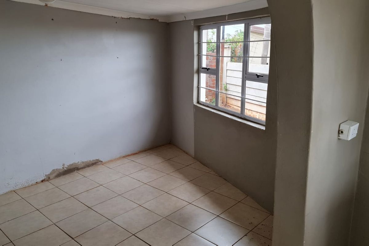An empty bedroom featuring tiled flooring, a window with security bars, and an arched entryway, currently requiring wall repairs and finishing.