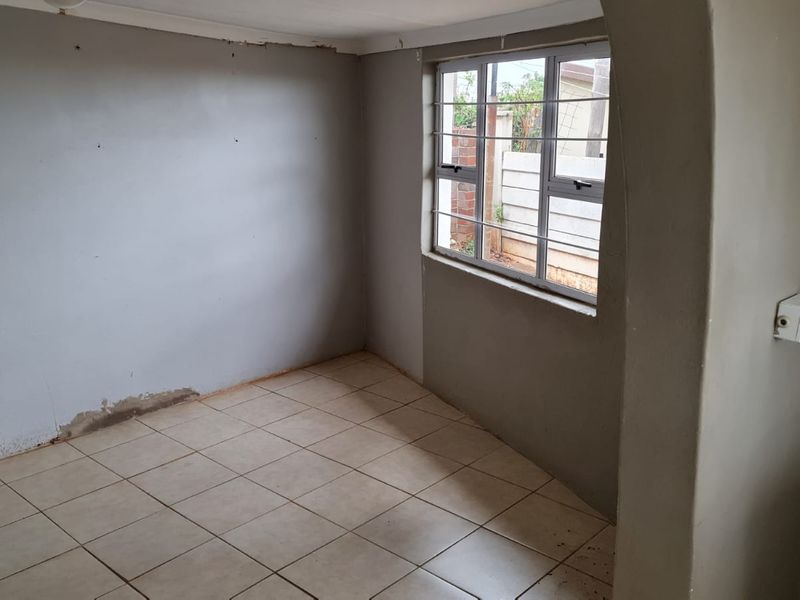 An empty bedroom featuring tiled flooring, a window with security bars, and an arched entryway, currently requiring wall repairs and finishing.