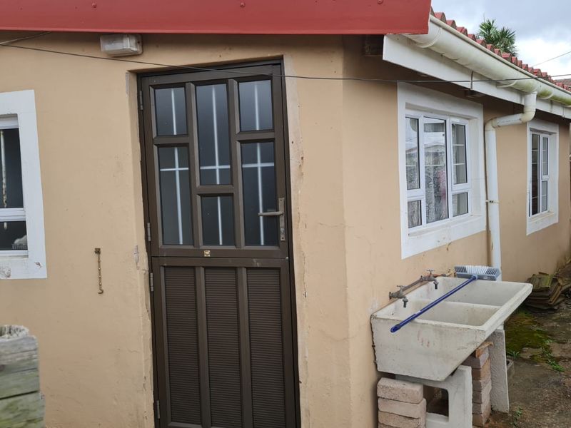 Rear exterior view of the property featuring a security door, aluminium windows, and a functional concrete laundry trough with external plumbing.