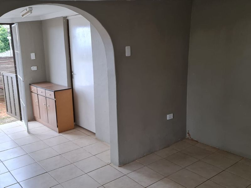 An empty living area featuring tiled flooring and a distinctive arched doorway leading to an exterior access point.