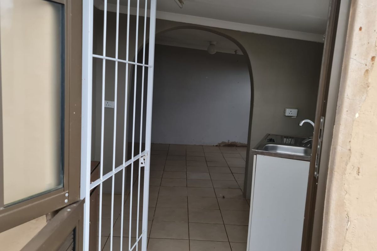 A compact, empty kitchen area featuring tiled flooring, a stainless steel sink, and an arched entryway leading to an adjacent room.