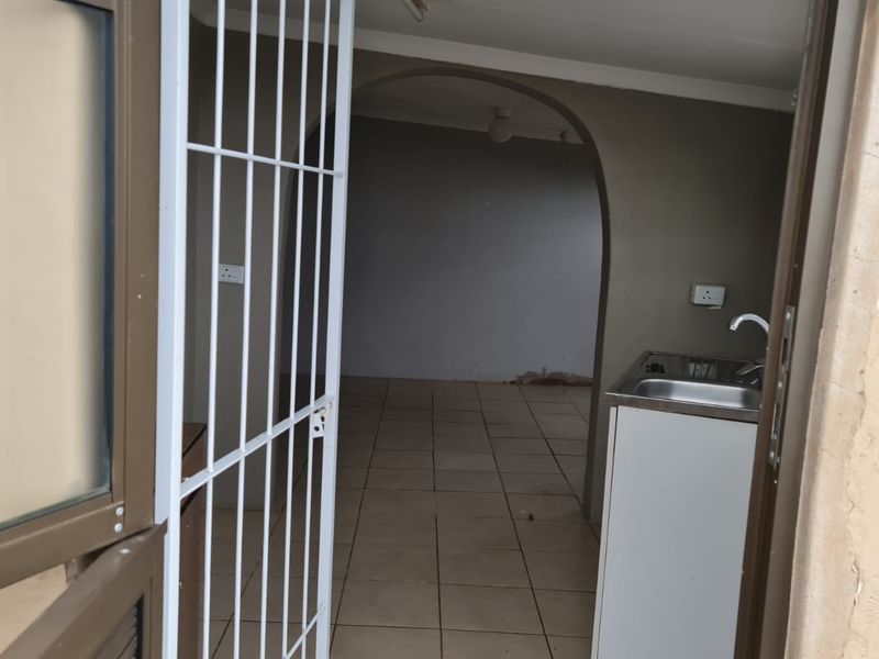 A compact, empty kitchen area featuring tiled flooring, a stainless steel sink, and an arched entryway leading to an adjacent room.