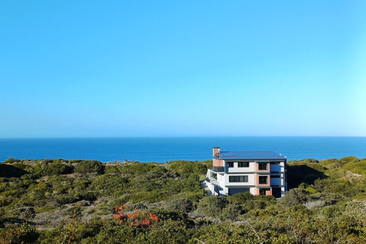 Aerial view of a modern multi-story house situated in a coastal landscape with ocean views.