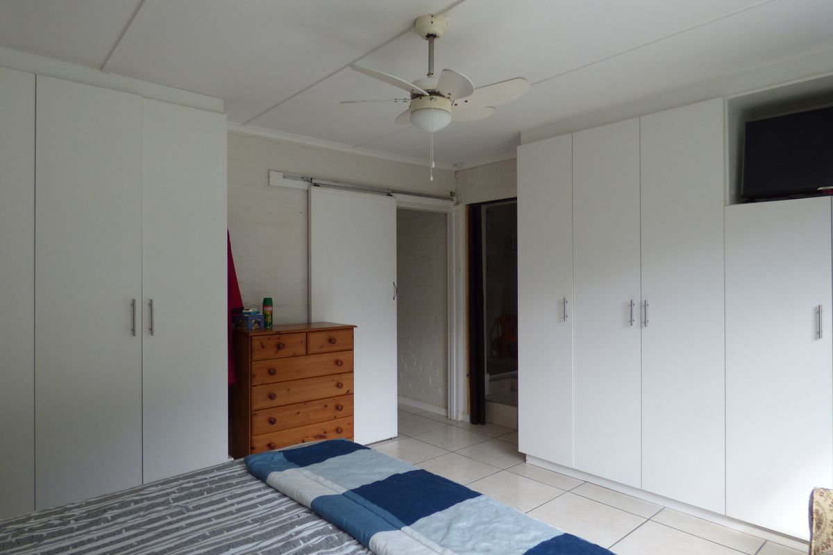 A bedroom featuring extensive white built-in cupboards, tiled flooring, and a ceiling fan, providing ample storage and functional living space.
