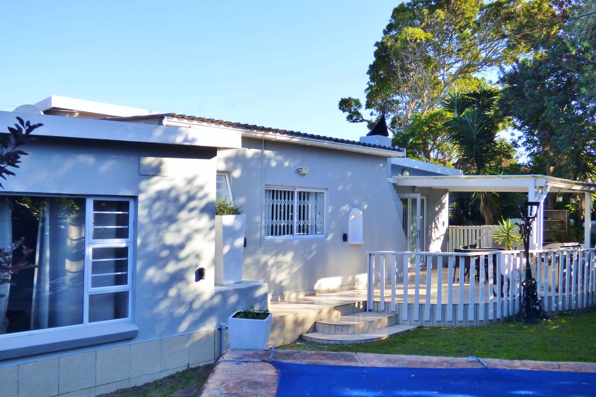 Rear view of the property featuring a tiled patio with timber balustrade, overlooking a swimming pool set within a landscaped garden.