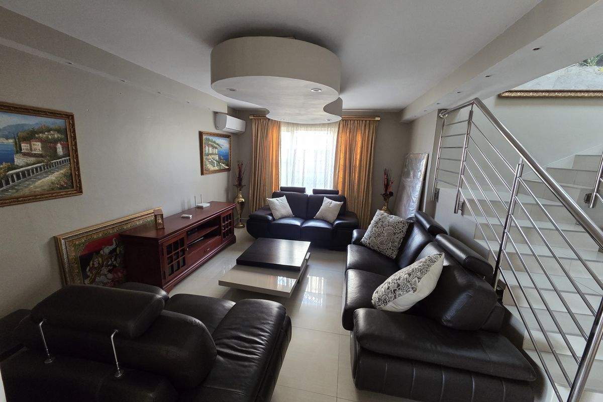 A well-maintained living room featuring tiled flooring, a unique recessed ceiling design, and a modern stainless steel staircase railing.
