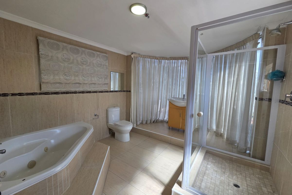 Spacious bathroom featuring a built-in corner bathtub, separate glass-enclosed shower, toilet, and a vanity basin with neutral wall and floor tiling.