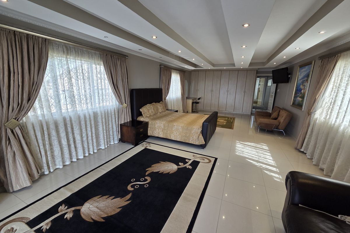 Spacious bedroom featuring a tray ceiling with recessed lighting, extensive built-in cupboards, and large windows with security bars.