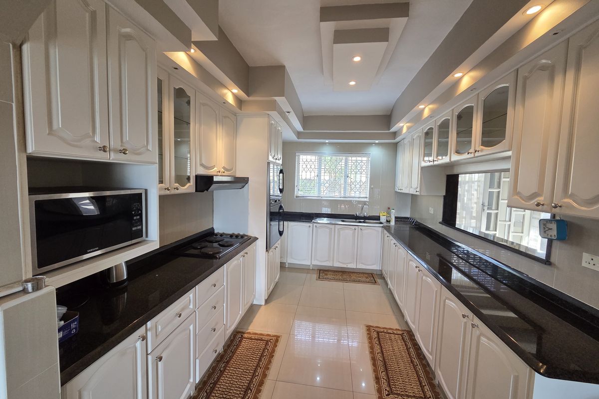 A well-maintained galley-style kitchen featuring white cabinetry, dark granite countertops, integrated appliances, and recessed ceiling lighting.